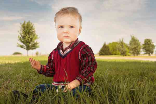 A photo of a small boy, sitting in a field, while wearing a sweater vest